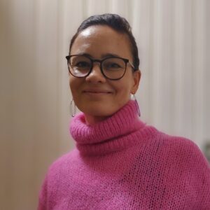 Tummatukkainen, silmälasipäivinen, pinkkiin jumpperiin pukeutunut nainen kasvokuvassa.