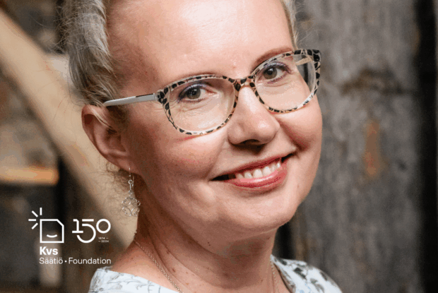 Vaaleatukkainen, muovisankaisiin silmälaseihin pukeutunut hymyilevä nainen tiukasti rajatussa kasvokuvassa.