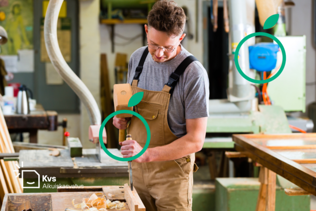 Nuori beesiin työhaalariin pukeutunut miesoletettu kumartuneena työstämään puuta työkalu kädessään taustallaan verstas.