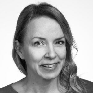 Hymyilevä vaaeatukkainen nainen rajatussa kasvokuvassa tukka toiselle olkapäälle aseteltuna.